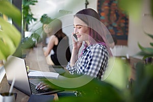 Side view of young businesswoman sitting at table in coffee shop. On table cup of coffee and laptop. In background white