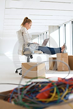 Side view of young businesswoman using laptop with feet up on cardboard box in office