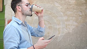 Side view of a young casual man drinking coffee while using phone