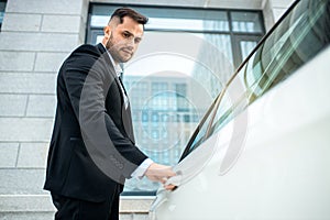 Side view on young caucasian man opening the door of luxurious car