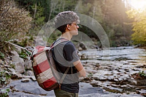 Side view on young Caucasian traveler with backpack standing in rural place at river.