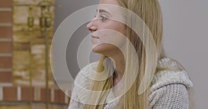 Side view of young Caucasian woman with blond hair and grey eyes looking away and smiling. Profile portrait of