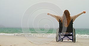 Side view of young Caucasian woman sitting with arms outstretched on wheelchair at beach 4kouple hav