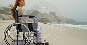 Side view of young Caucasian woman sitting on wheelchair at beach 4k