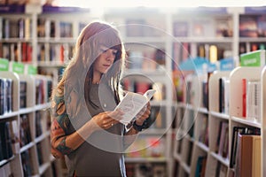 Side view of young Caucasian woman with tattoo posing reading book in bookstore. Concept of education and shopping