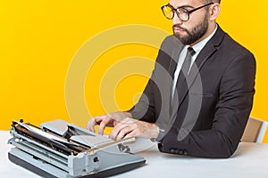 Side view of a young charming male businessman in formal attire and glasses typing on a typewriter text. Concept of