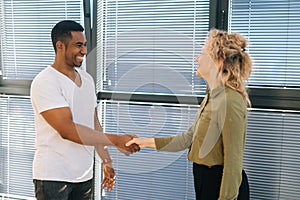 Side view of young cheerful Caucasian businesswoman having conversation with smiling African American male colleague by