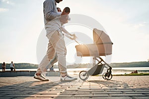 Side view. A young couple with a baby pram is walking together