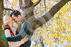 Side view of young couple hugging near autumn tree in park