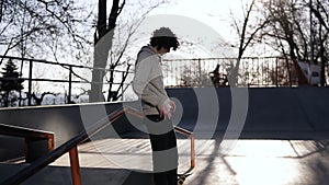 Side view of a young curly headed male skateboarder browsing in his mobile phone in the skate park on a sunny day. Lean