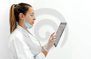 Side view of a young doctor using a tablet with the mask down in her clinic