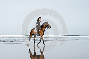 side view of young female equestrian riding horse on sandy