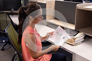 Side view of young female hispanic advisor analyzing chart while working at modern workplace