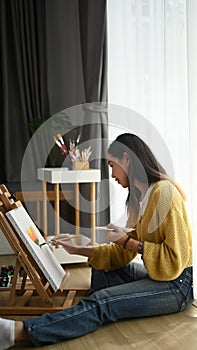 Side view of a young female painter painting in her workshop.