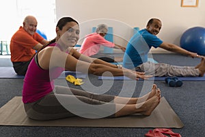 Side view of young female trainer exercising with senior people