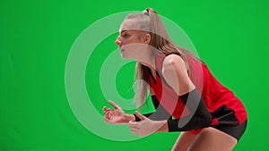 Side view of young female volleyball player hitting the ball on a green screen. Athlete in red uniform waiting for the