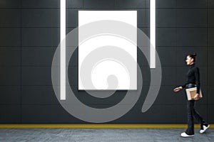 Side view of female walking in modern grunge hallway interior with empty white mock up banner. Subway passage concept