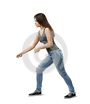 Side view of young fit woman in gray top and blue jeans bending forward slightly and posing as if holding invisible rope