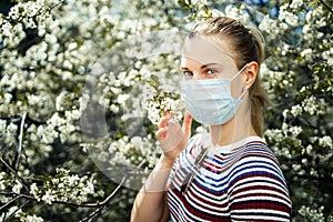 Side view of young girl in medical mask on background of blossoming apple tree on summer day.