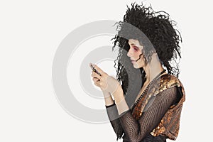 Side view of young Goth woman with teased hair texting on mobile phone over gray background