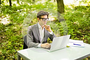 Side view of Young handsome business man working at laptop at office table in green park. Business concept.