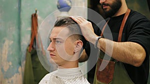 Side view of young handsome caucasian man with piercing in his ear getting his hair dressed and styled by a bearded