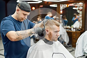 Side view of a young handsome man visiting barbershop and getting new trendy haircut. Barber working with hair clipper