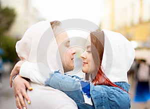 Side view of a young happy couple in love, men and women in hoods in the summer on the street.