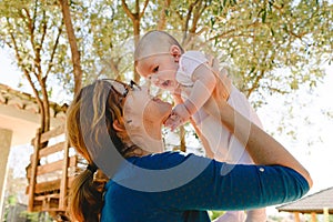 Side view Young happy mom playing raising her newborn baby to make her laugh