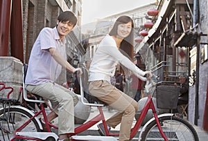 Side View of Young Heterosexual Couple on a Tandem Bicycle in Beijing Looking at Camera photo