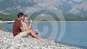 Side view of young interethnic couple relaxing on pebble beach. Travel concept.