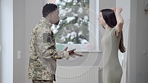 Side view of young interracial couple arguing shouting and gesturing indoors. Stressed African American military man and