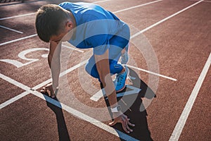 Side view of young male athlete at starting block on running track. Caucasian sprinter man in starting position for running to