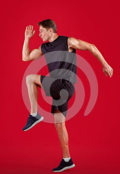 Side view of young male sprinter running, exercising on red studio background