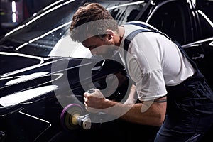 Side view on young man auto mechanic worker polishing car at automobile repair and renew service station shop