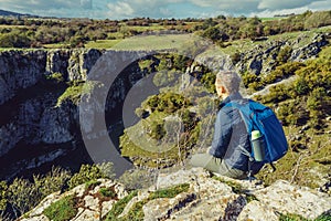 Side view young man hiker with backpack sitting on mountain`s top enjoying rocks landscape background. Travel lifestyle wanderlus