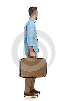 Side view of young man holding luggage and leaving town