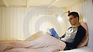 Side view a young man is lying on a bed and working on a laptop, typing on a keyboard, working at night, remote work