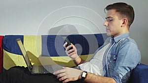 Side view a young man is lying on the sofa and working on a laptop, typing on the keyboard, remote work from home.