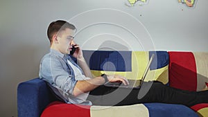 Side view a young man is lying on the sofa and working on a laptop, typing on the keyboard, remote work from home.