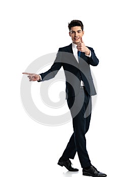 side view of young man pointing finger to side and making thumbs up gesture