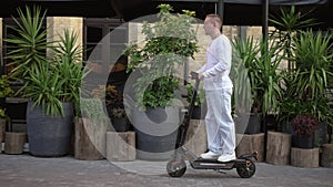 Side view young man riding e-scooter on city street on spring summer day. Wide shot portrait of Caucasian confident