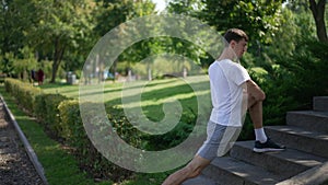 Side view young man stretching leg muscles in slow motion outdoors. Concentrated inspired Caucasian sportsman warming up