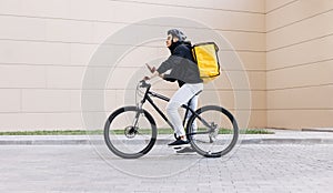 Side view of a young messenger with termal backpack man riding his bike and using mobile phone in the city photo