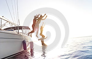 Side view of young millennial friends jumping from sailboat on sea ocean trip - Guys and girls having summer fun together