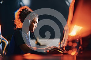 Side view of a young mixed race girl, female cybersport gamer wearing headphones playing online video games