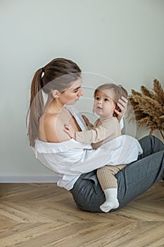 Side view of young mother sitting on floor at home and holding little beautiful baby daughter