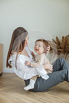 Side view of young mother sitting on floor at home and holding little beautiful baby daughter