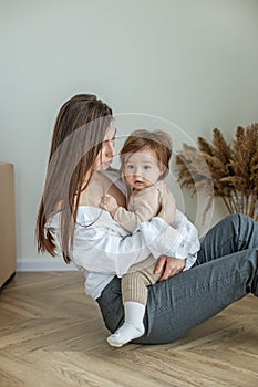 Side view of young mother sitting on floor at home and holding little beautiful baby daughter