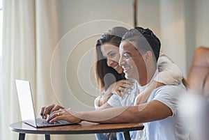 Side view of young people using laptop at home with happiness. Boy and girl living together and working on a notebook computer
